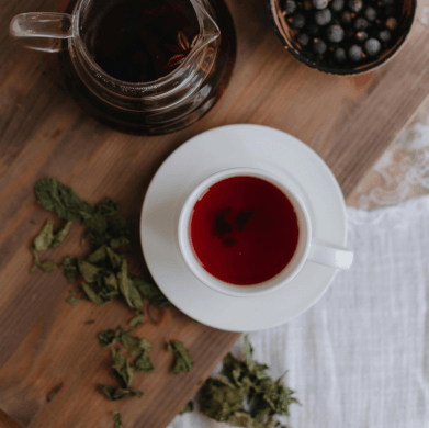 Tasse mit Cannabistee auf einem Holztisch. Um den Tee liegen getrocknete Cannabisblüten.