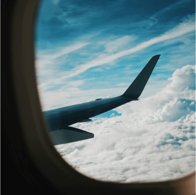 Blick aus dem Fenster eines Flugzeug auf den Flügel. Leicht bewölkter, blauer Himmel.