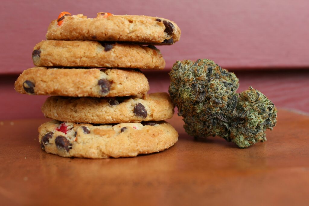 Mehrere Schoko-Cookies liegen gestapelt neben einer getrockneten Cannabisblüte. Das Bild zeigt beispielhaft die Vielfalt moderner Cannabisprodukte, von essbaren Varianten bis zur klassischen Blüte, wie sie im Blogbeitrag zur Entwicklung und Legalität von Cannabisprodukten in Deutschland thematisiert wird.