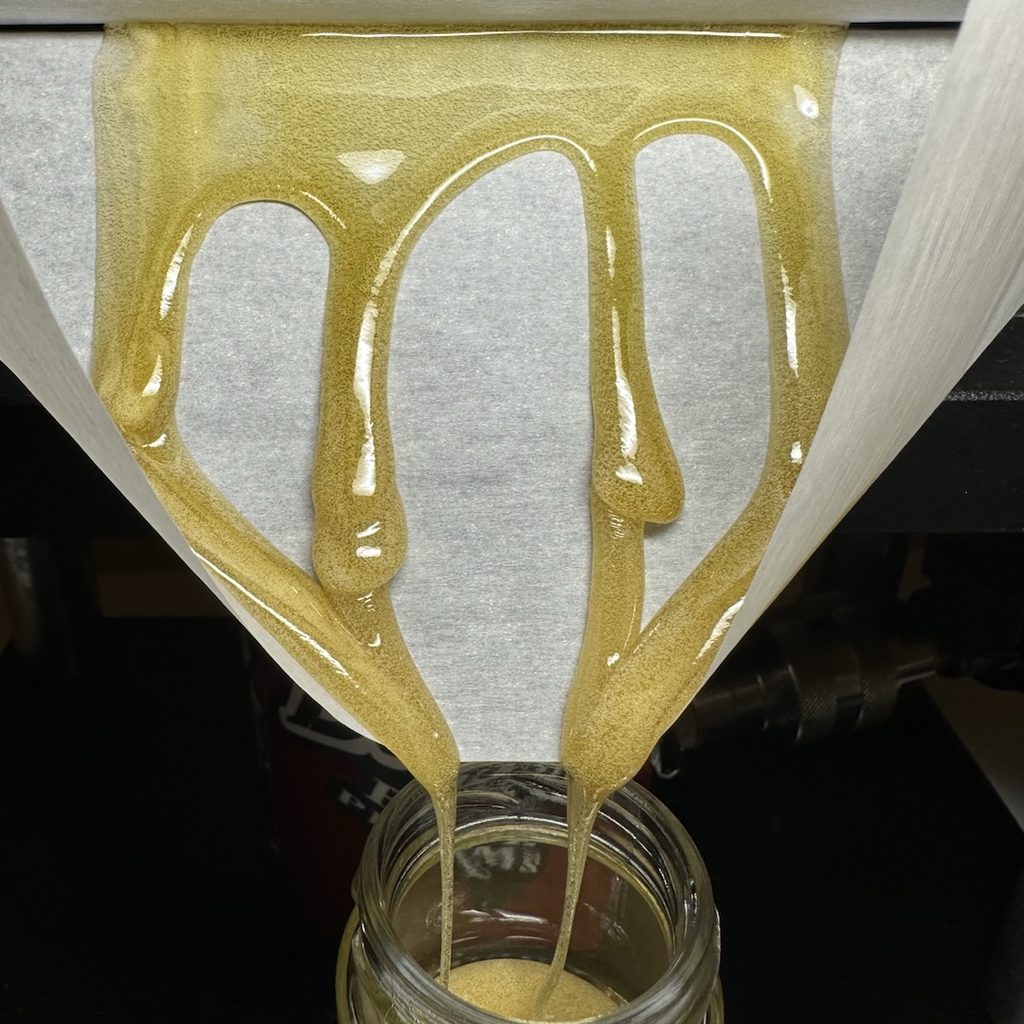 Frisch gepresstes Hash-Rosin läuft über Backpapier in ein Glasbehälter.