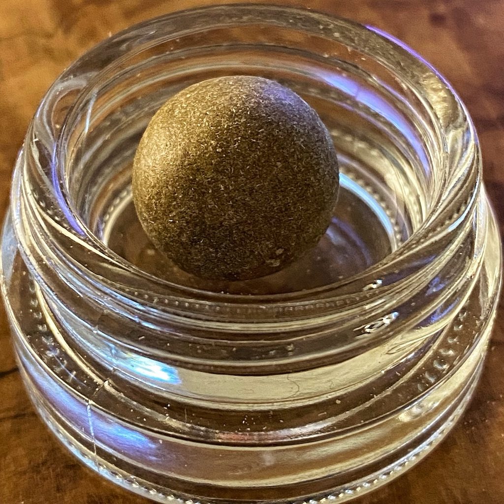Ein kleine, braune Kugel Temple Ball Haschisch in einem kleinen Glasbehälter.